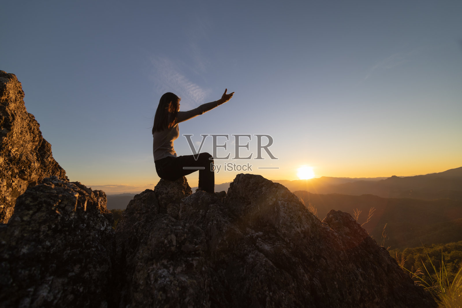 一个女人坐在岩石上的剪影张开手掌感谢上帝。希望理念，相信上帝，希望美好的生活。照片摄影图片