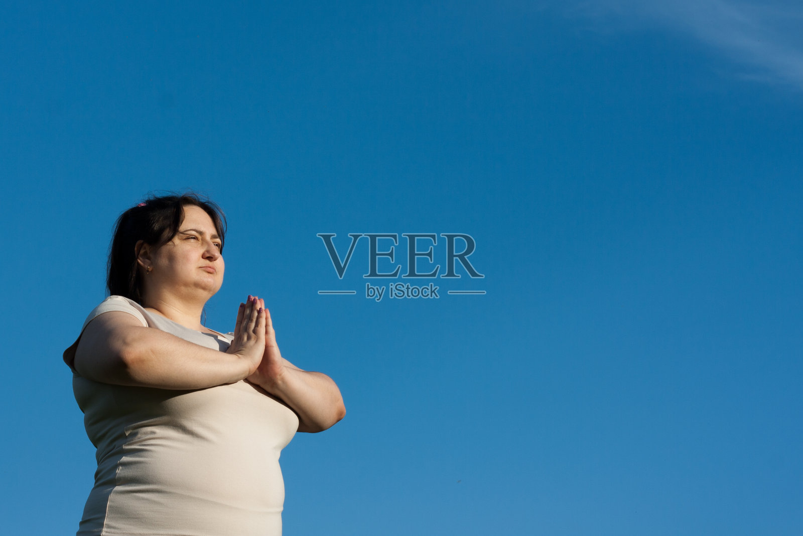 平静的女人在冥想时双手合十，蓝天背景。照片摄影图片
