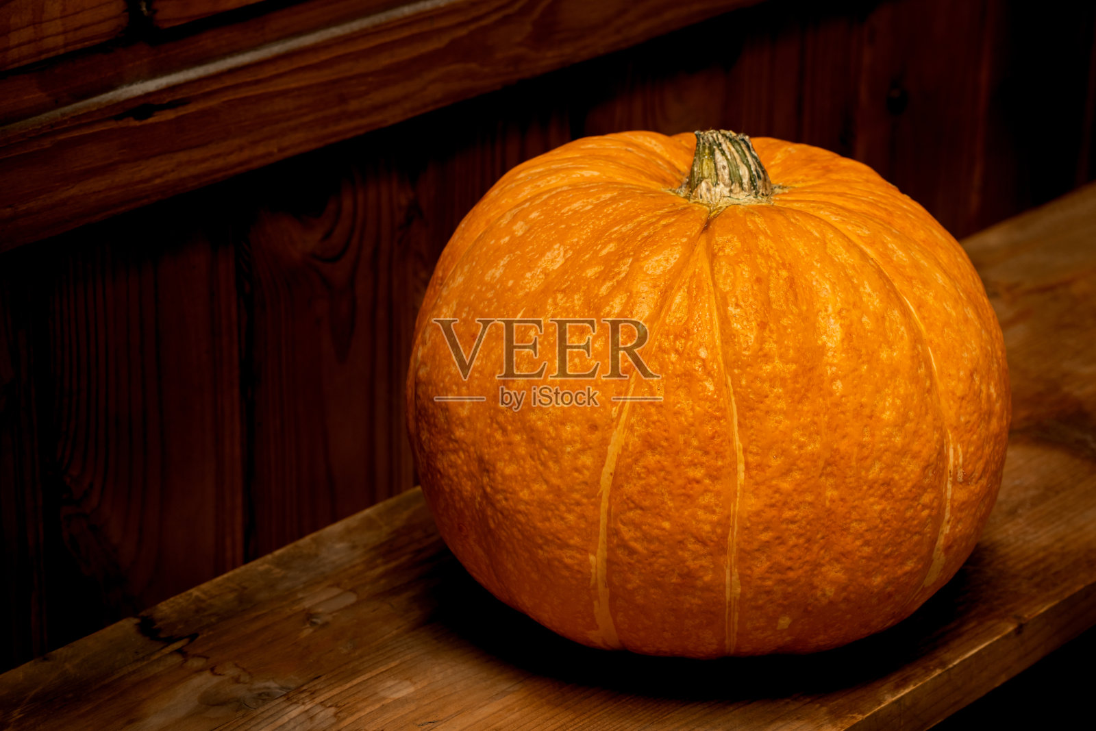 一个橙色的南瓜躺在一个黑暗的谷仓的架子上。照片摄影图片