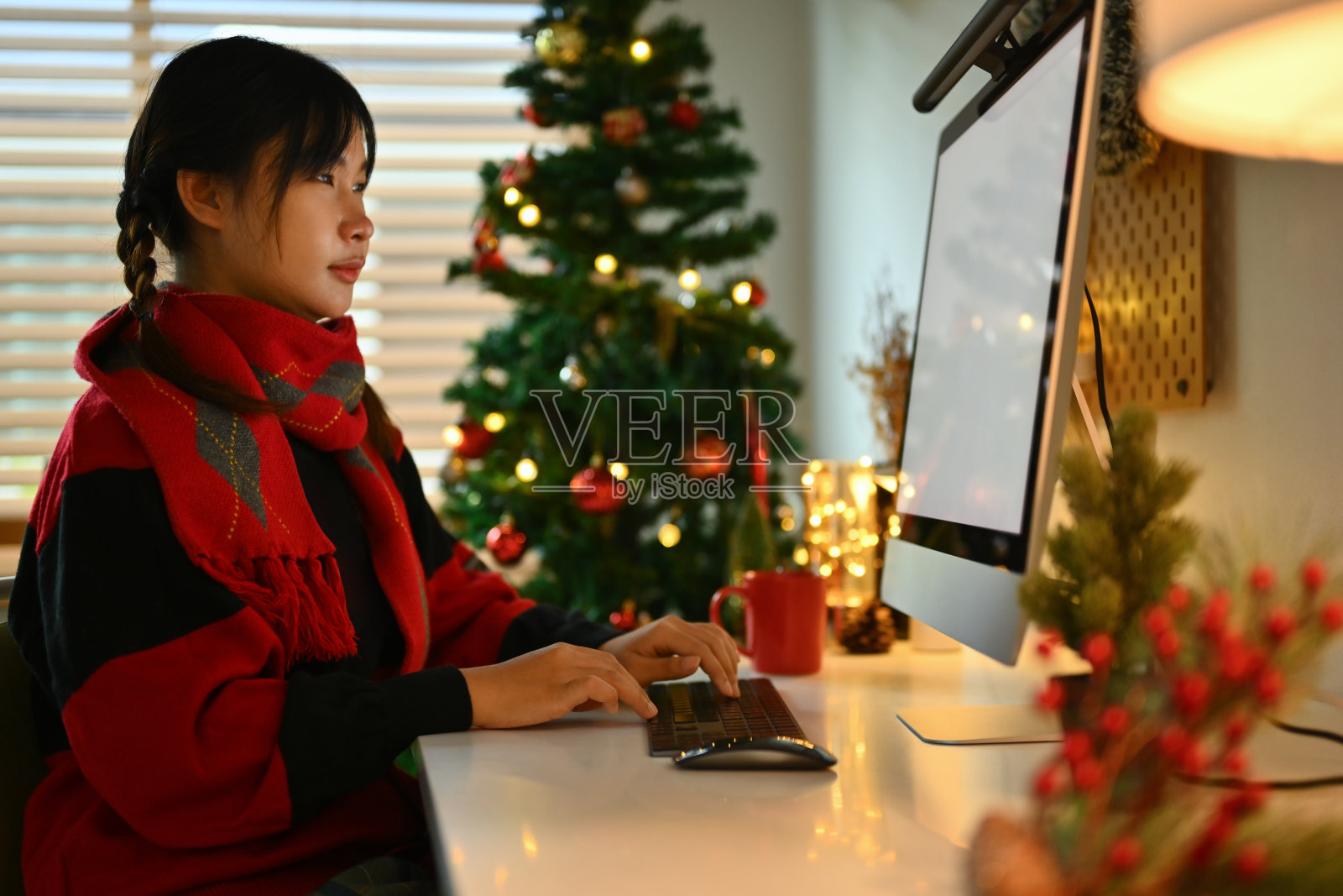 年轻女子穿着温暖舒适的针织毛衣坐在装饰圣诞树和电脑照片摄影图片
