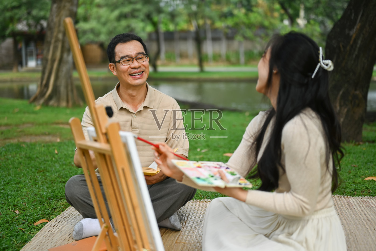 快乐的50多岁的男人和年轻的成年女儿在公园的绿草地上画画照片摄影图片