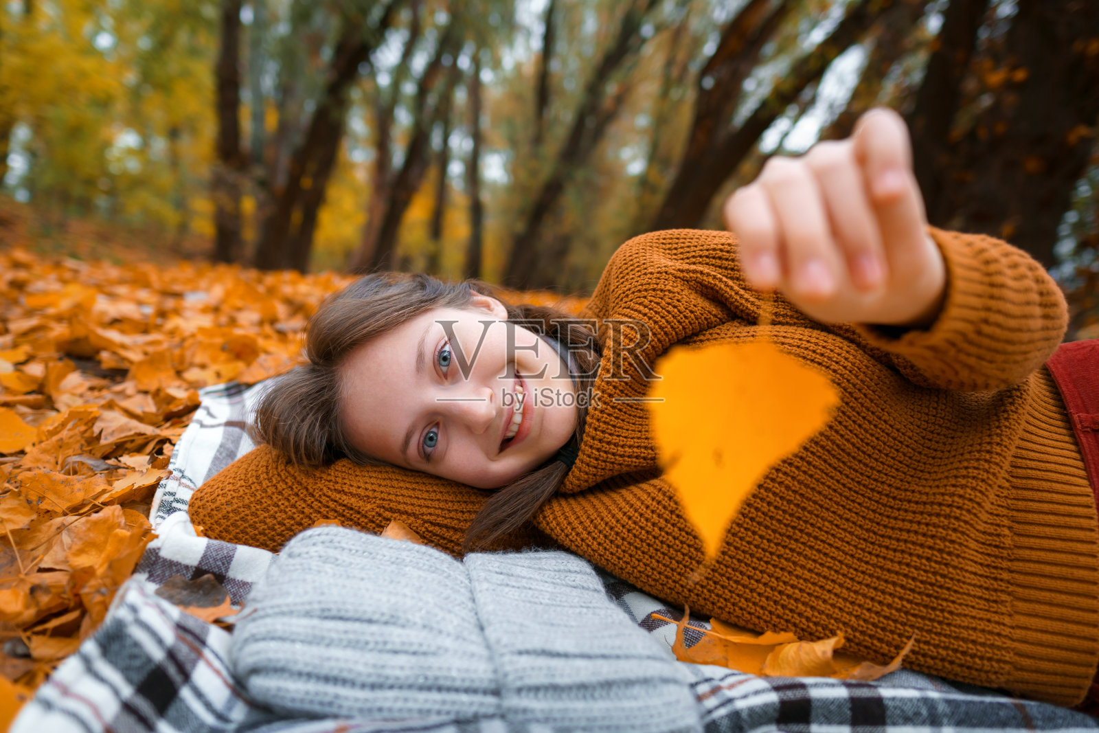 一个十几岁的小女孩躺在秋天森林的河边空地上，欣赏着美丽的大自然和嫩黄的树叶照片摄影图片
