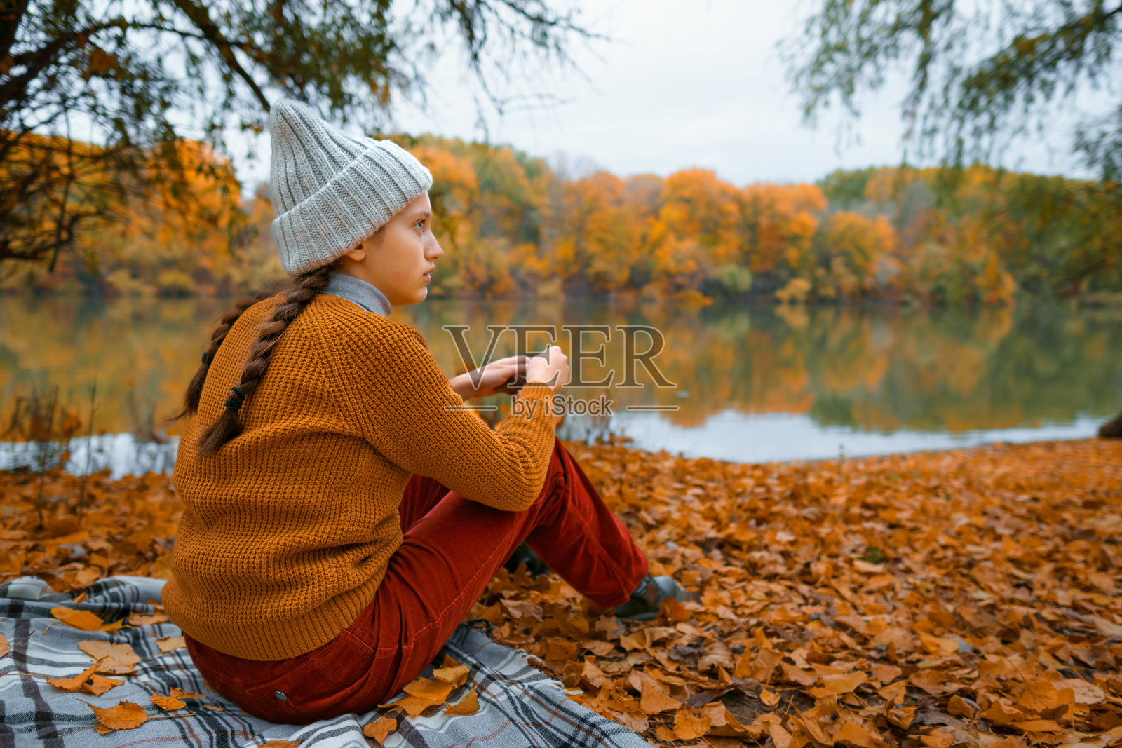 一个十几岁的小女孩坐在秋天森林里河边的空地上，欣赏着美丽的大自然和嫩黄的树叶照片摄影图片