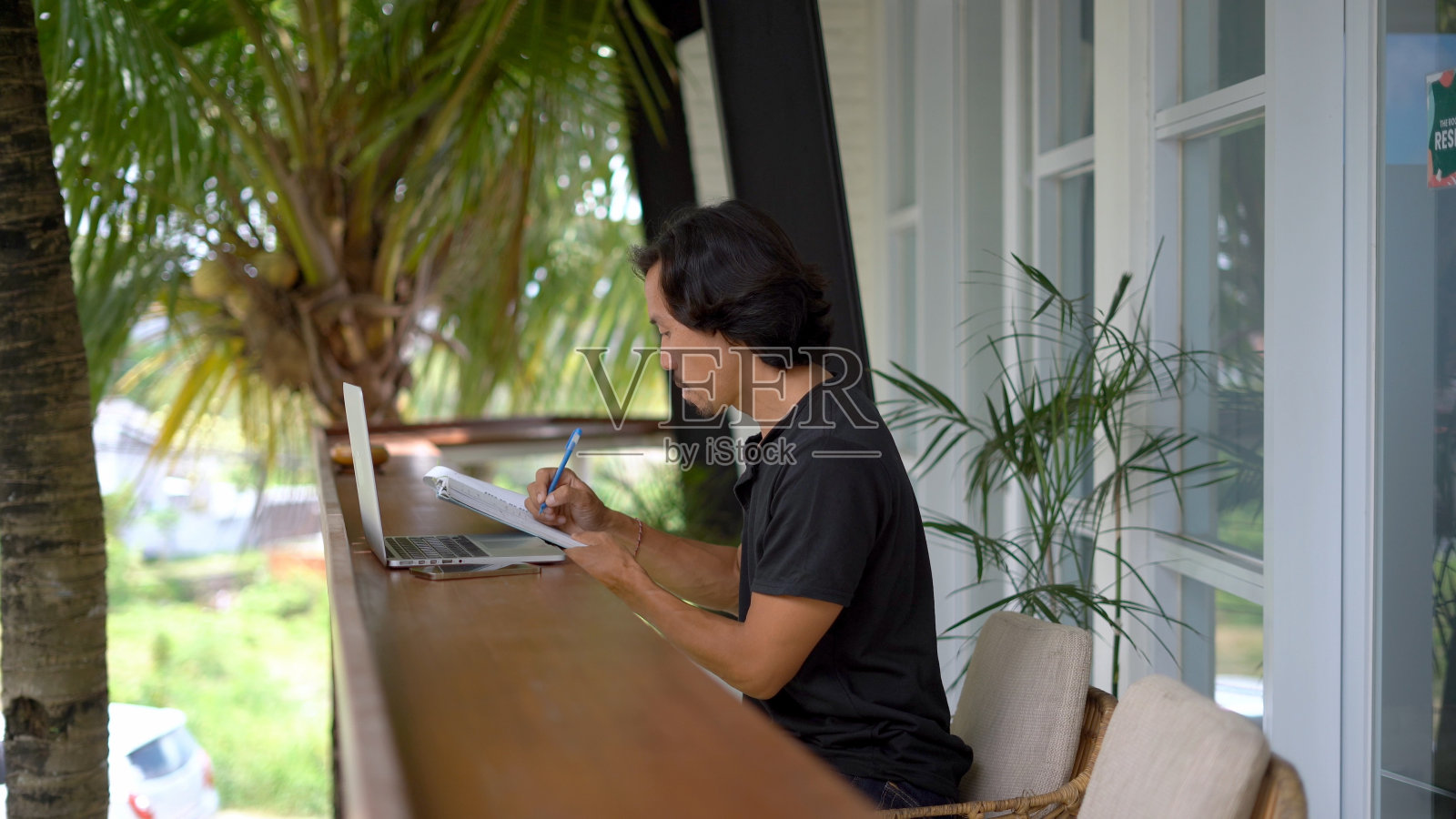 一名亚洲男子在咖啡馆外写笔记本。自由职业者在线互联网工作。照片摄影图片