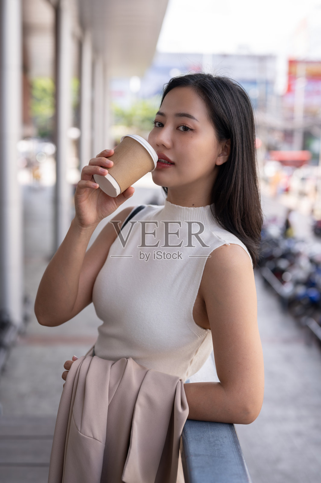 一位迷人的千禧一代亚洲女性在城市里散步时喝着咖啡。照片摄影图片