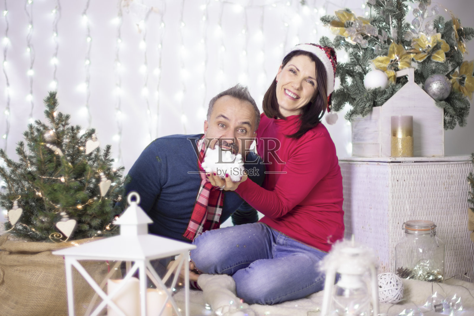 一个女孩和一个男孩穿着圣诞服装在镜头前摆姿势，笑着玩雪，背景是一棵装饰好的圣诞树。圣诞装饰。情侣们玩得开心照片摄影图片