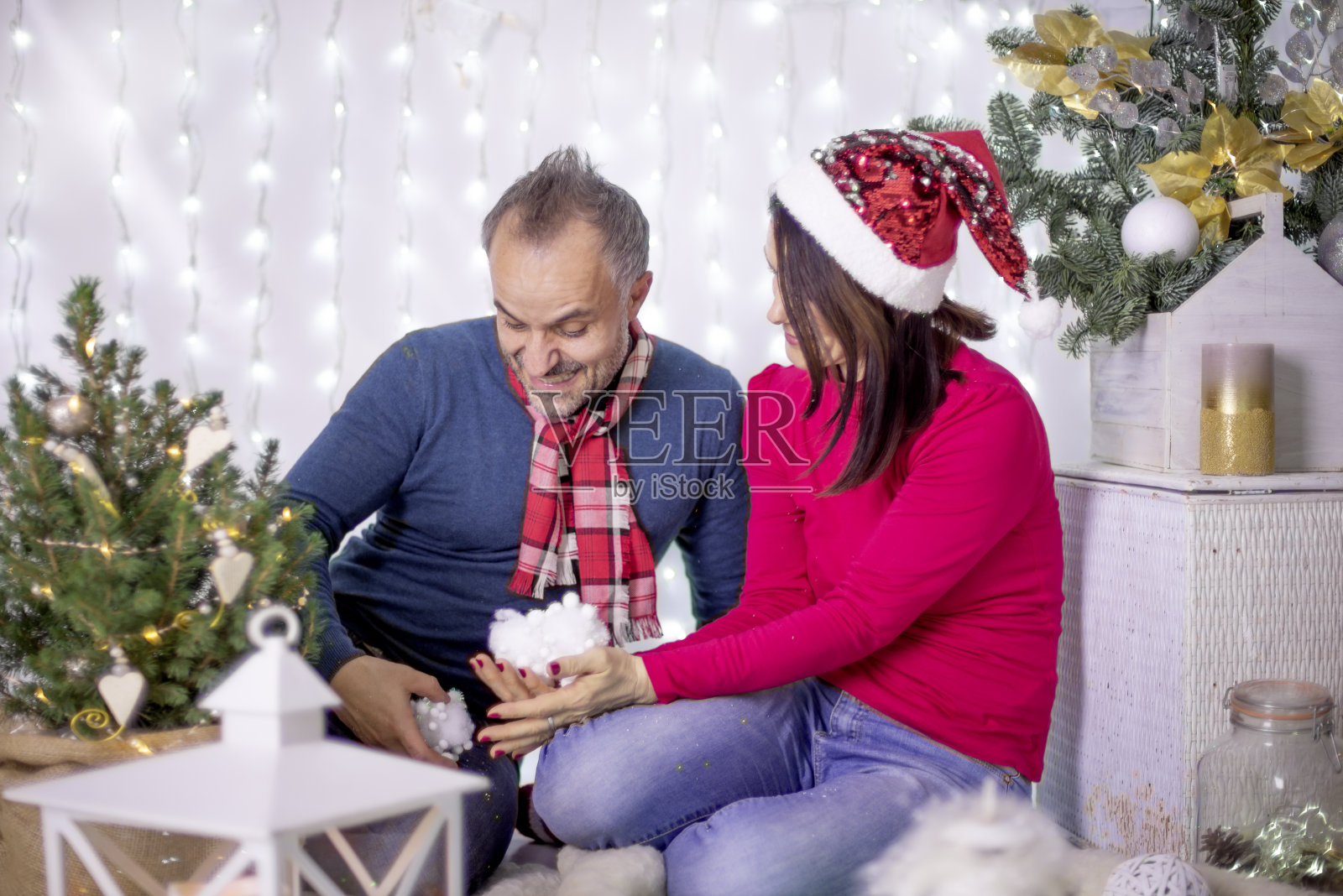 一个男孩和一个女孩穿着圣诞服装，手里拿着人造雪，笑着，在圣诞装饰的节日装饰中玩耍，背景是模糊的灯光。和朋友一起拍节日全家福照片摄影图片