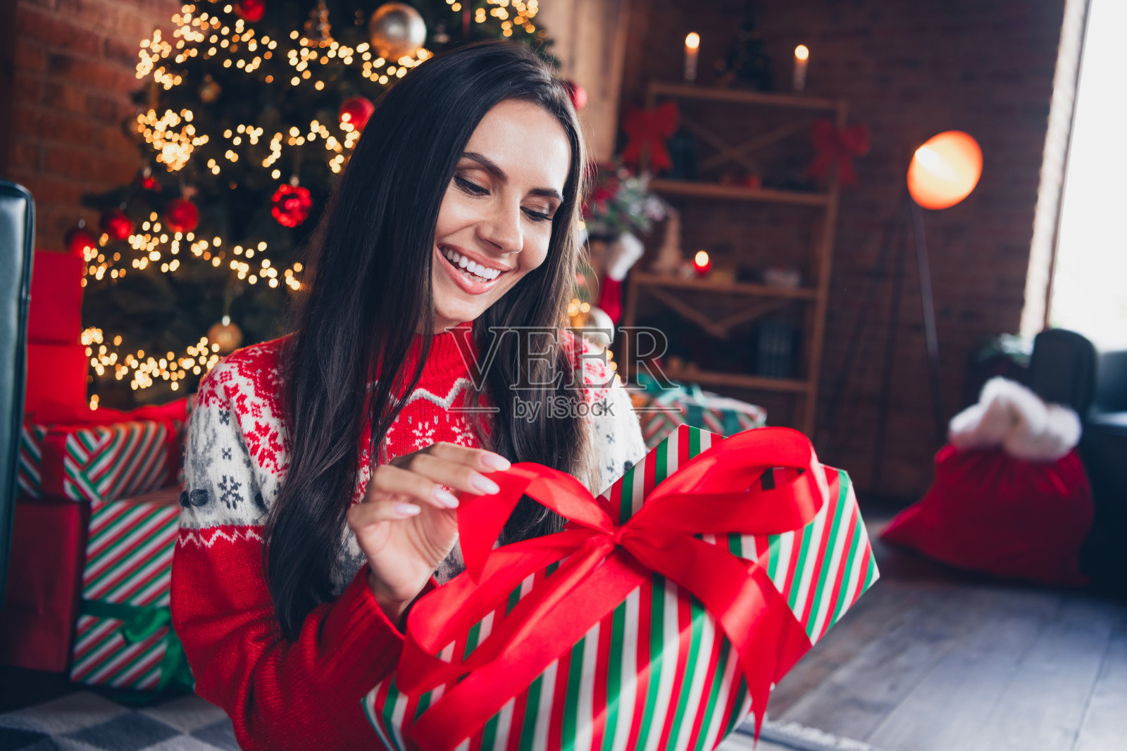 心情愉快的漂亮女孩穿着红色印花套头衫，在室内拿着拆包惊喜礼物照片摄影图片