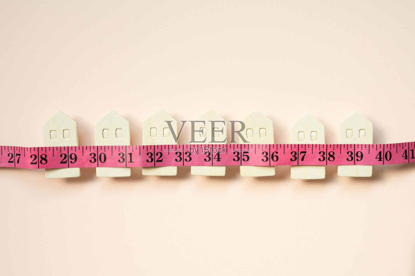 粉红色背景上的微型木样板房和卷尺。租赁、购买、房地产的概念照片摄影图片