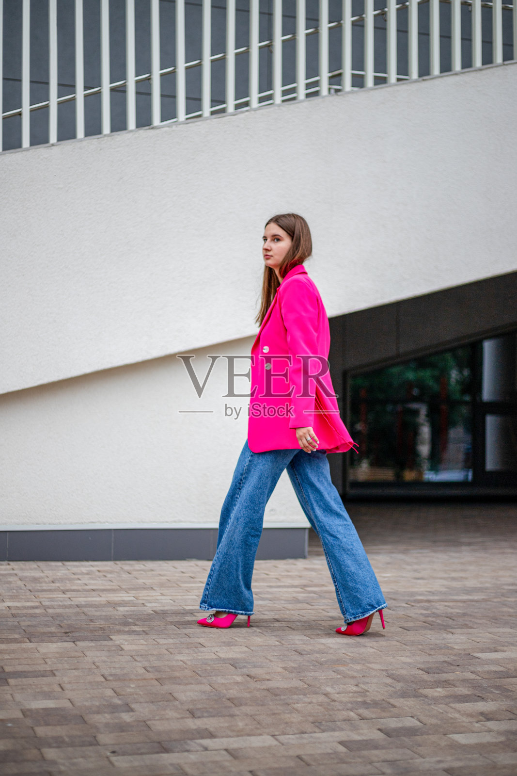 一个年轻的商务女孩穿着一件色彩鲜艳的夹克，把夹克拉下来，穿着牛仔裤走在街上照片摄影图片