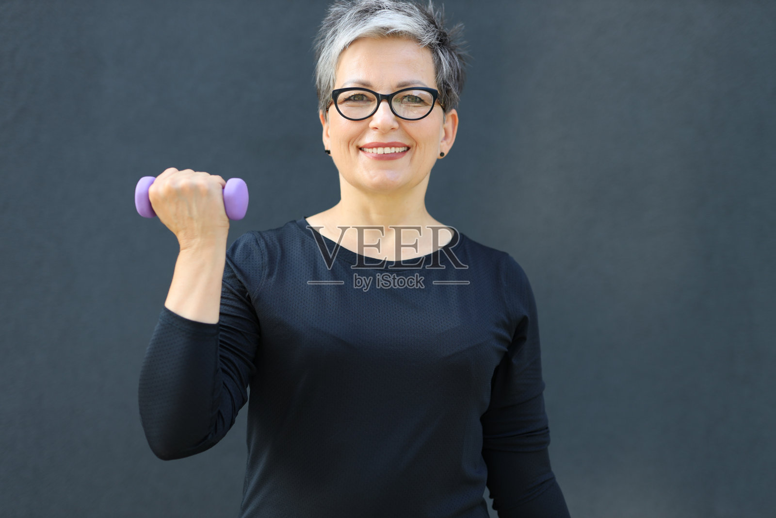 一个快乐健康的60多岁的成熟女性，拥有积极而充满活力的生活方式，一边举哑铃一边带着愉快的微笑享受户外健身。照片摄影图片