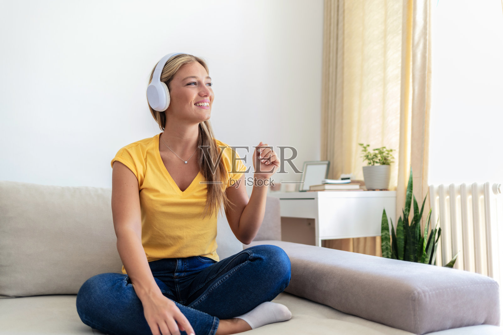 美女坐在家里的沙发上，戴着耳机，用智能手机听音乐。照片摄影图片