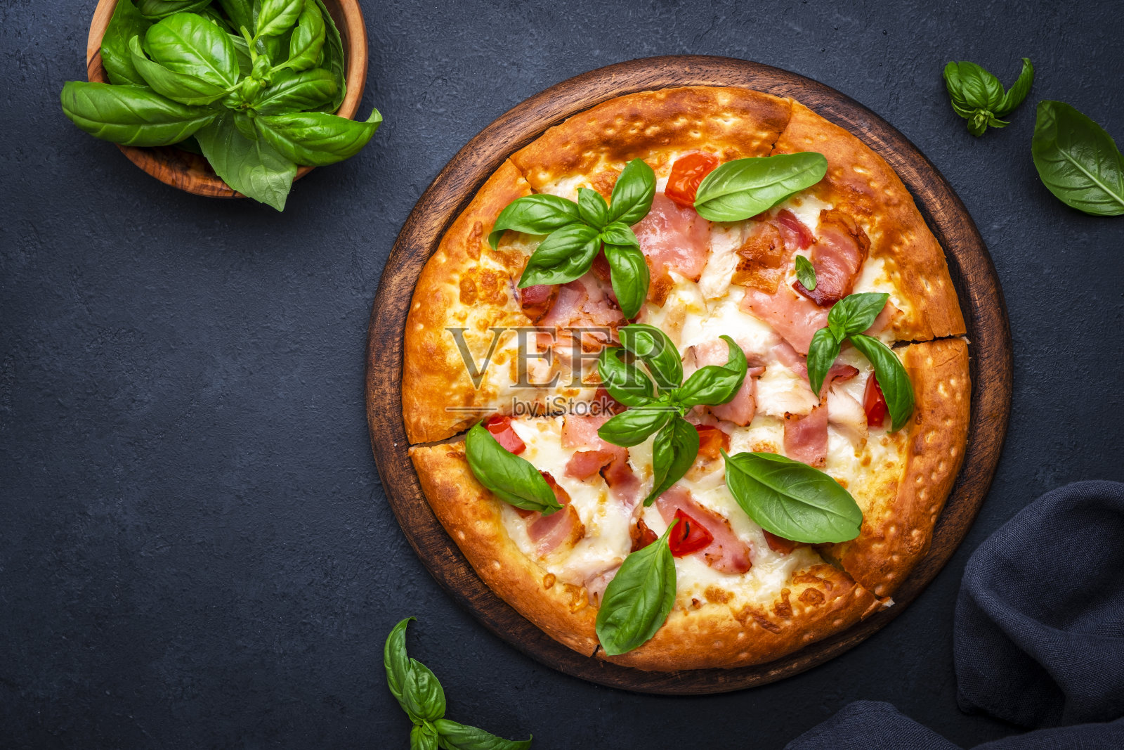自制热披萨，配烟熏火腿、奶酪、辣味番茄酱和绿色罗勒，黑色餐桌背景，俯视图照片摄影图片