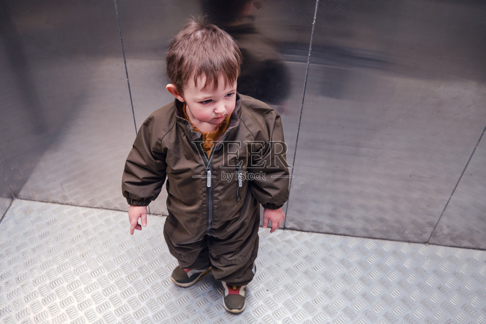 悲伤的宝宝站在公寓楼的电梯里。一个小孩坐在家里的电梯里。两岁左右(一岁十个月)照片摄影图片