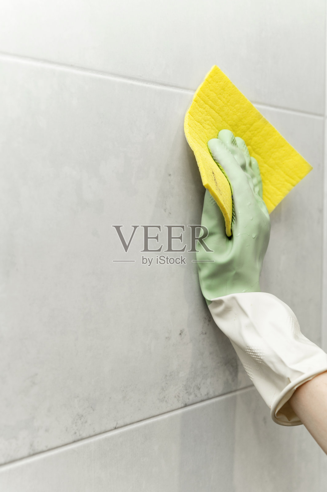 洗墙上的瓷砖。一个戴着橡胶手套的女性手的特写，用黄色的抹布清洗墙上的瓷砖照片摄影图片