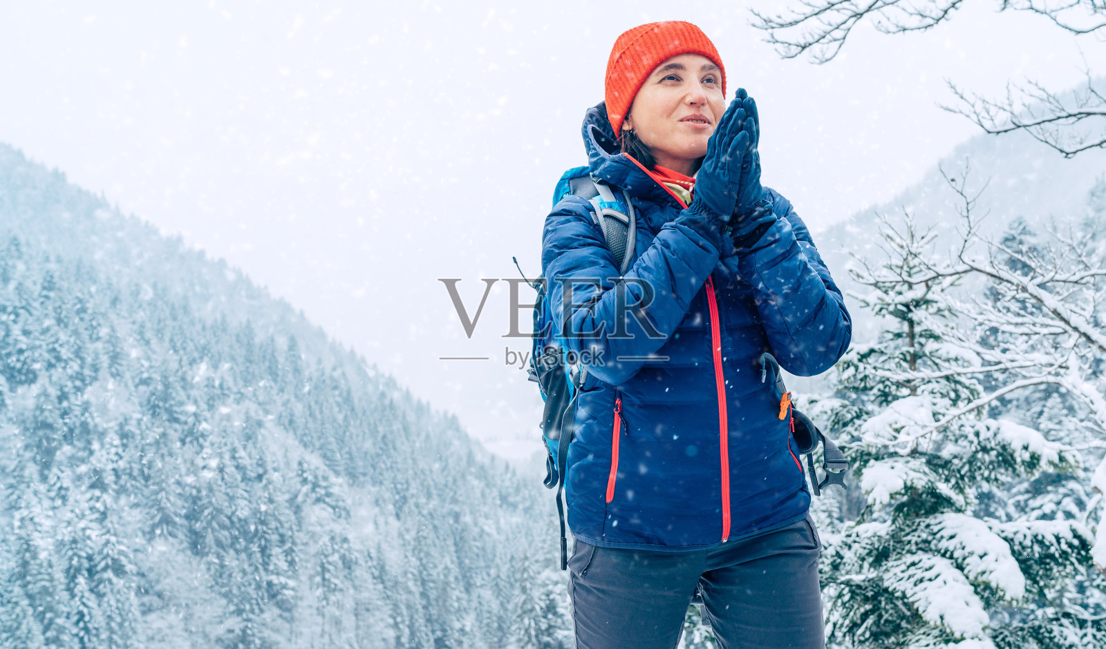 女背包客穿着温暖的羽绒服，背着双肩包，在冬季的山林路线上，温暖着手掌，欣赏着雪山风景。积极的人在大自然的概念。照片摄影图片