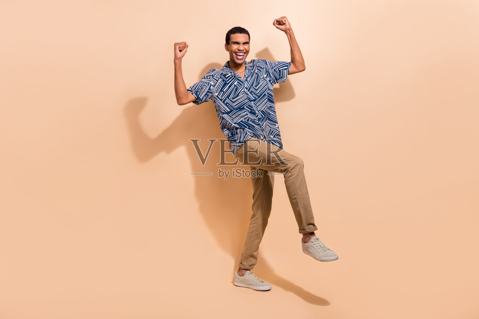 全身照片的幸运兴奋的男人穿着印花衬衫走上升的手臂拳头孤立米色背景照片摄影图片