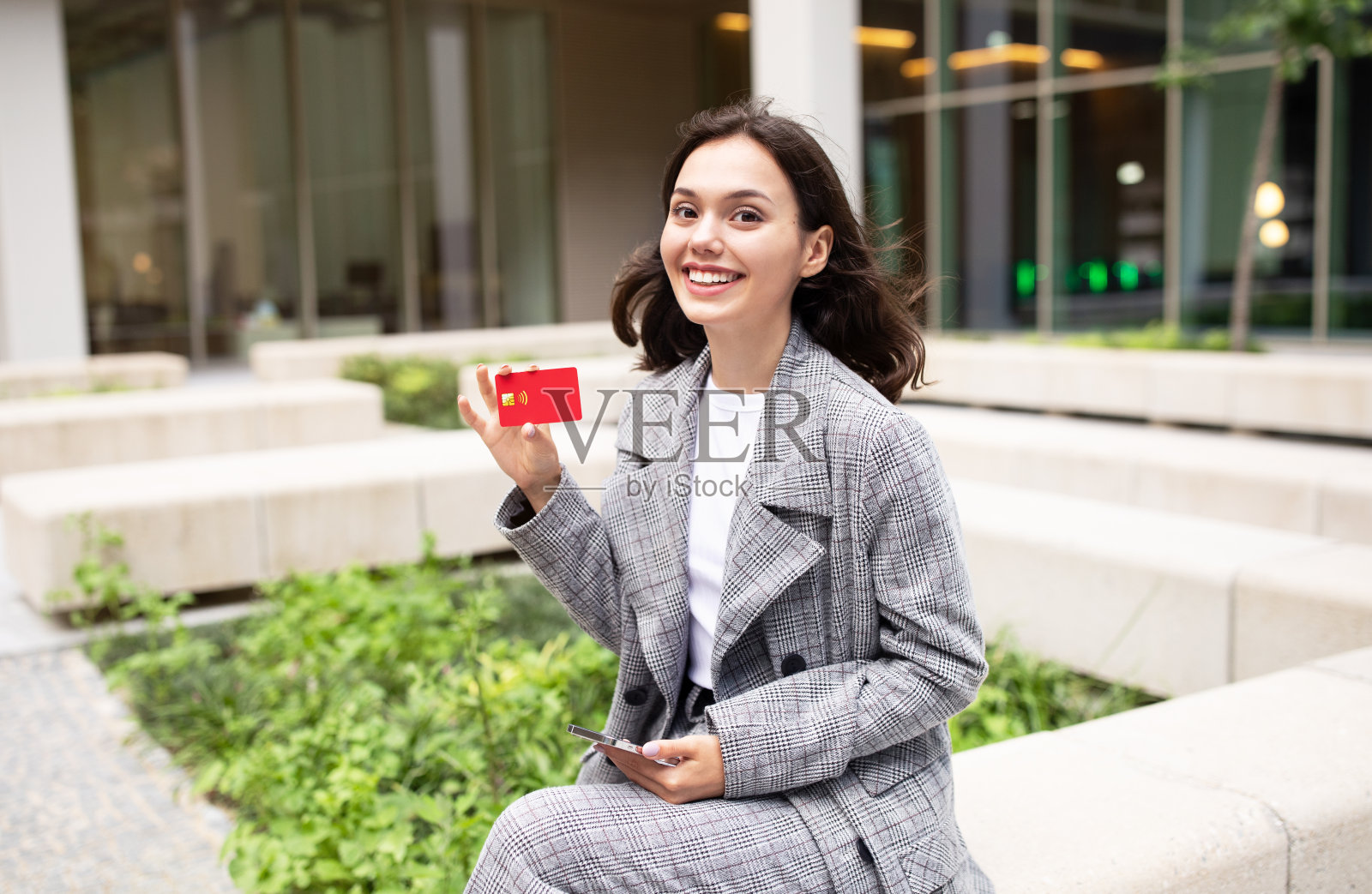 在市区，一名妇女手持手机展示信用卡照片摄影图片