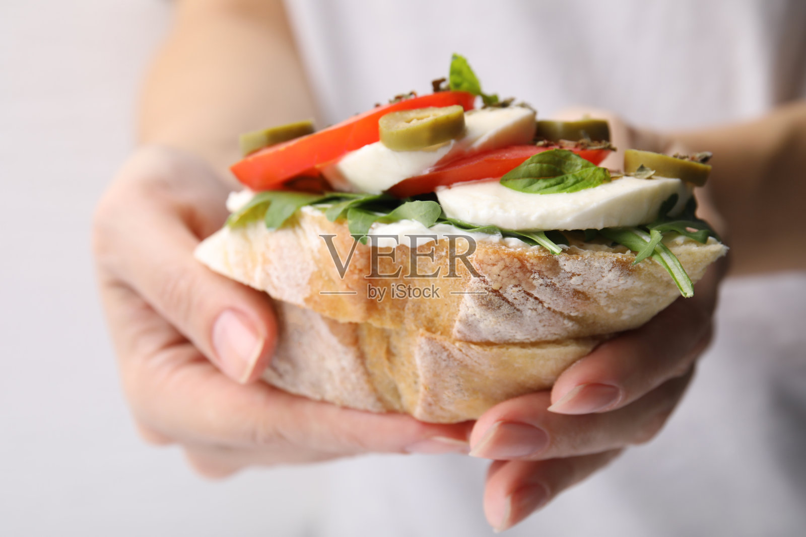 一个女人拿着美味的意式烤面包，上面有西红柿、马苏里拉奶酪和橄榄，背景是白色的，特写照片摄影图片