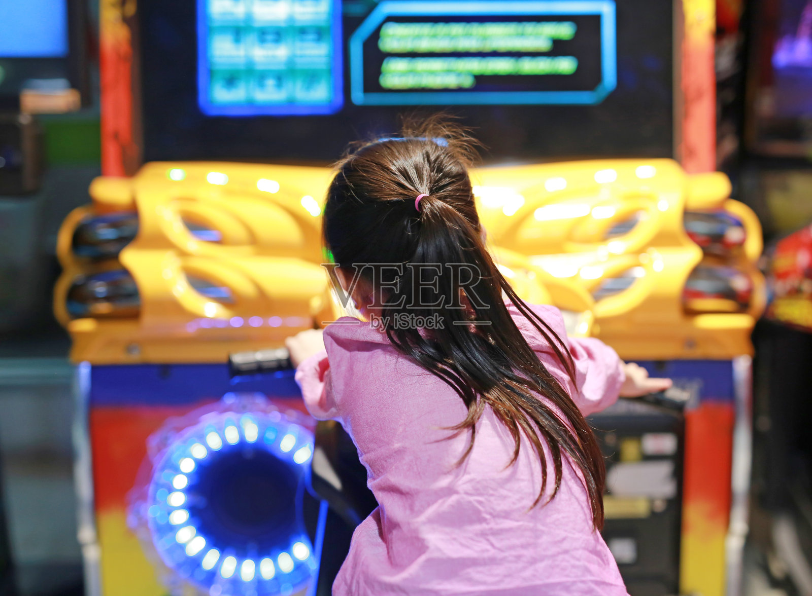 亚洲小女孩玩街机电子游戏的后视图。摩托车赛车。照片摄影图片