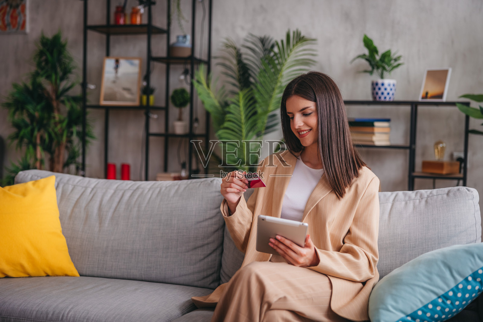 漂亮的年轻女子坐在家里的沙发上使用平板电脑照片摄影图片