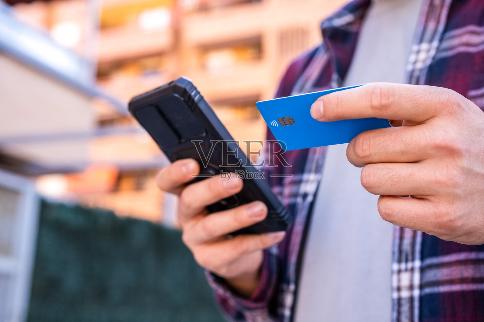 一个年轻人用银行卡和智能手机在城市街道上进行网上购物。照片摄影图片