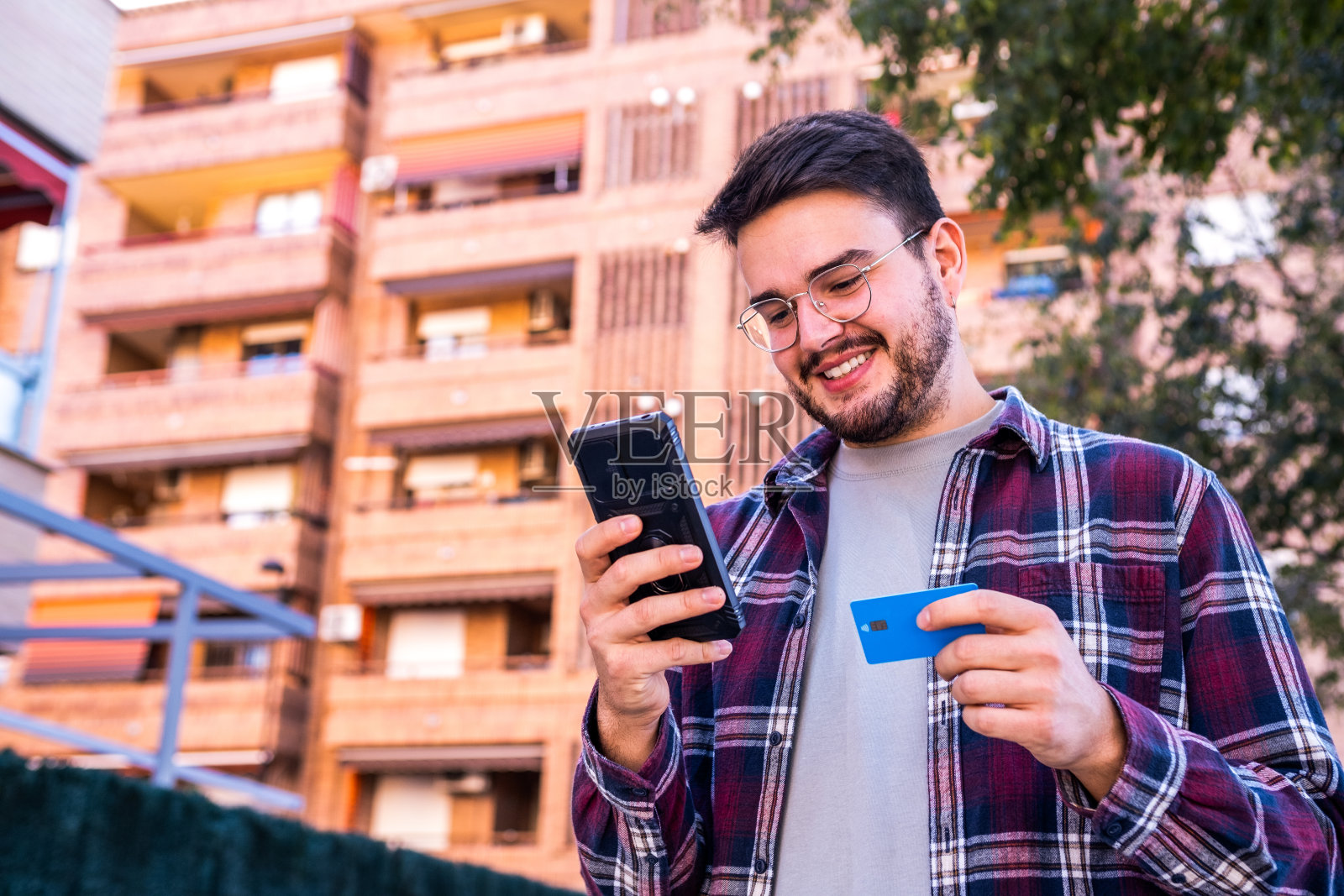 一个年轻人用银行卡和智能手机在城市街道上进行网上购物。照片摄影图片