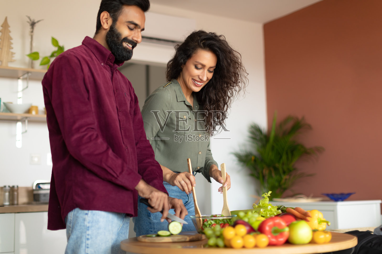 健康营养理念：阿拉伯夫妇在厨房一起烹饪新鲜蔬菜沙拉照片摄影图片