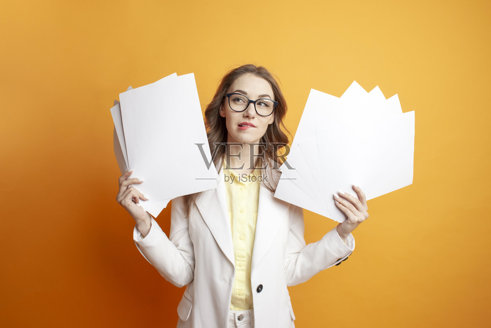 穿着白色西装的沉思女商人拿着橙色背景的文件，戴眼镜的女经理拿着文件照片摄影图片