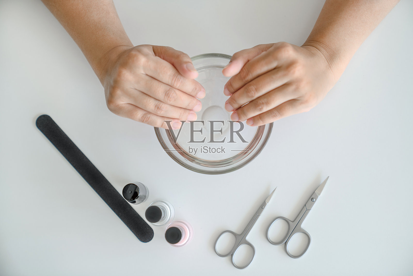 女人的手用温水和有用的物质洗澡。指甲锉、剪刀和几瓶清漆是桌子上的下一个，俯视图。指甲及手部护肤概念照片摄影图片