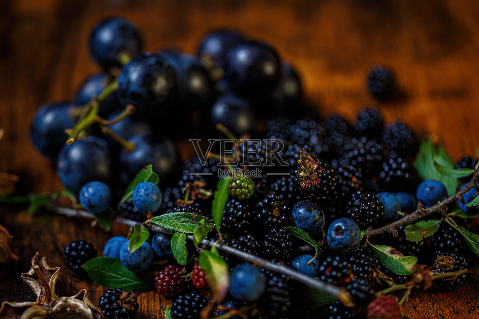 木桌上的浆果、蓝莓葡萄。绿叶和干花。浅景深。带有散景的黑暗模糊背景。照片摄影图片