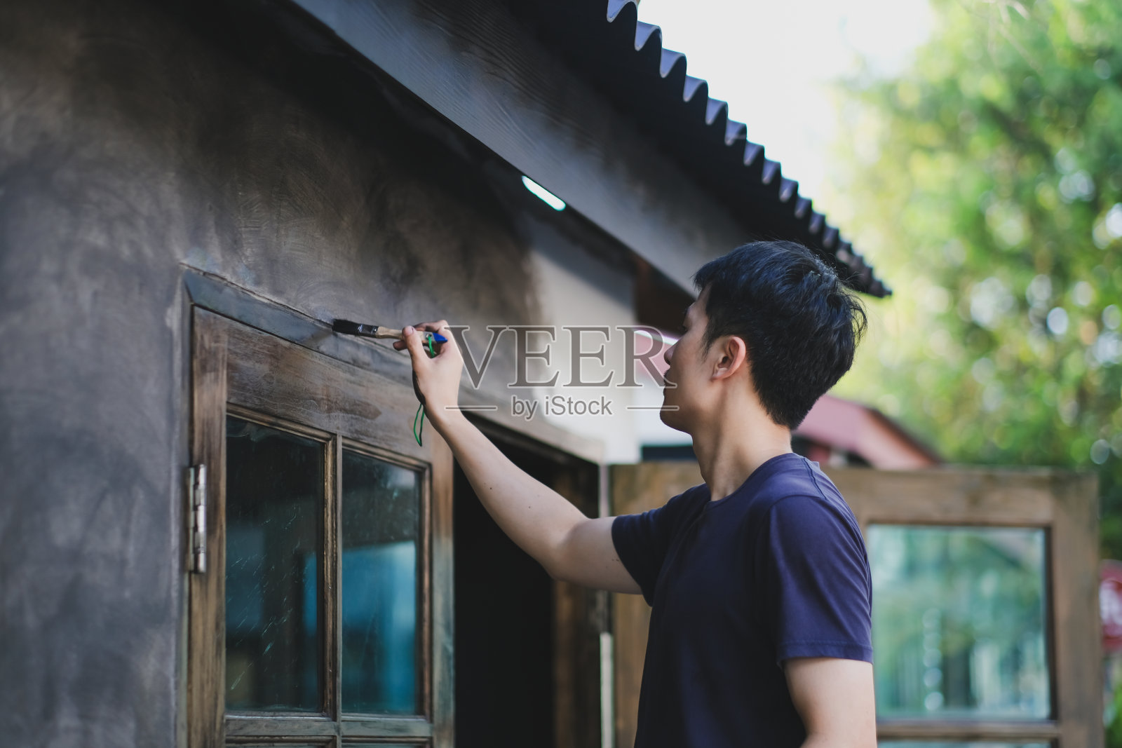 店主正在翻新和装饰他的商店，用画笔在他前面的商店的墙上画画。开心微笑的亚洲帅哥本地创业餐厅。照片摄影图片