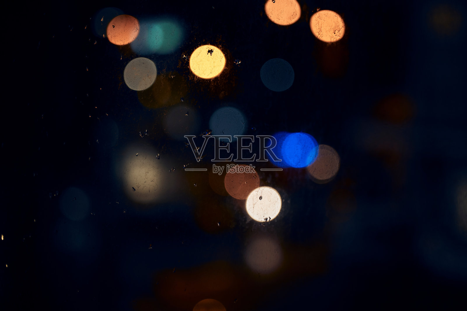 散景，夜晚和光线在一个窗户上与水滴，液体或水分对一个黑暗的抽象背景。迷离的灯光，五彩缤纷，雨滴或飞溅在玻璃上，为雨季的城市景观照片摄影图片