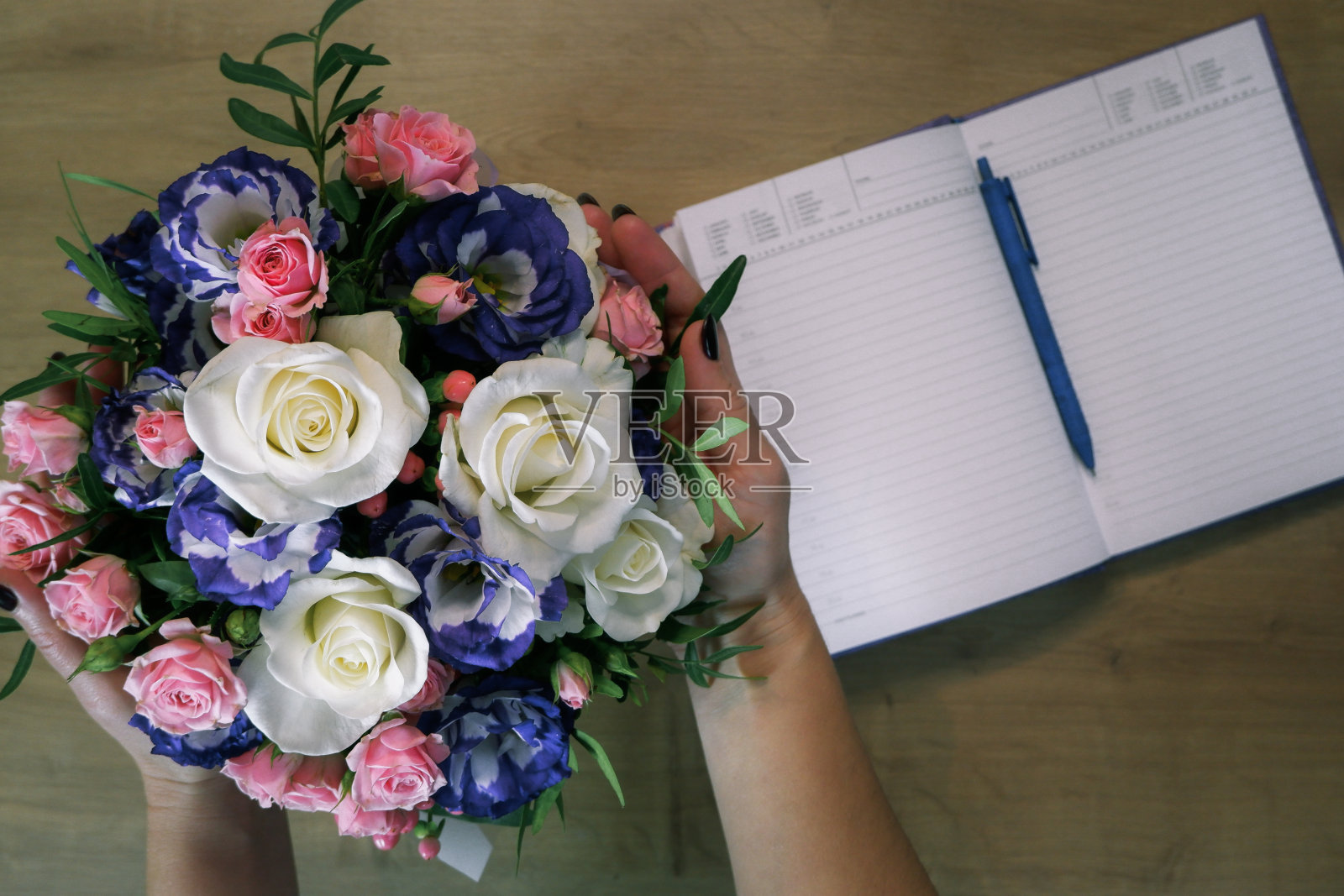 Flatlay。女性手中捧着一束五颜六色的玫瑰花。笔记本，在木桌上用笔写日记照片摄影图片