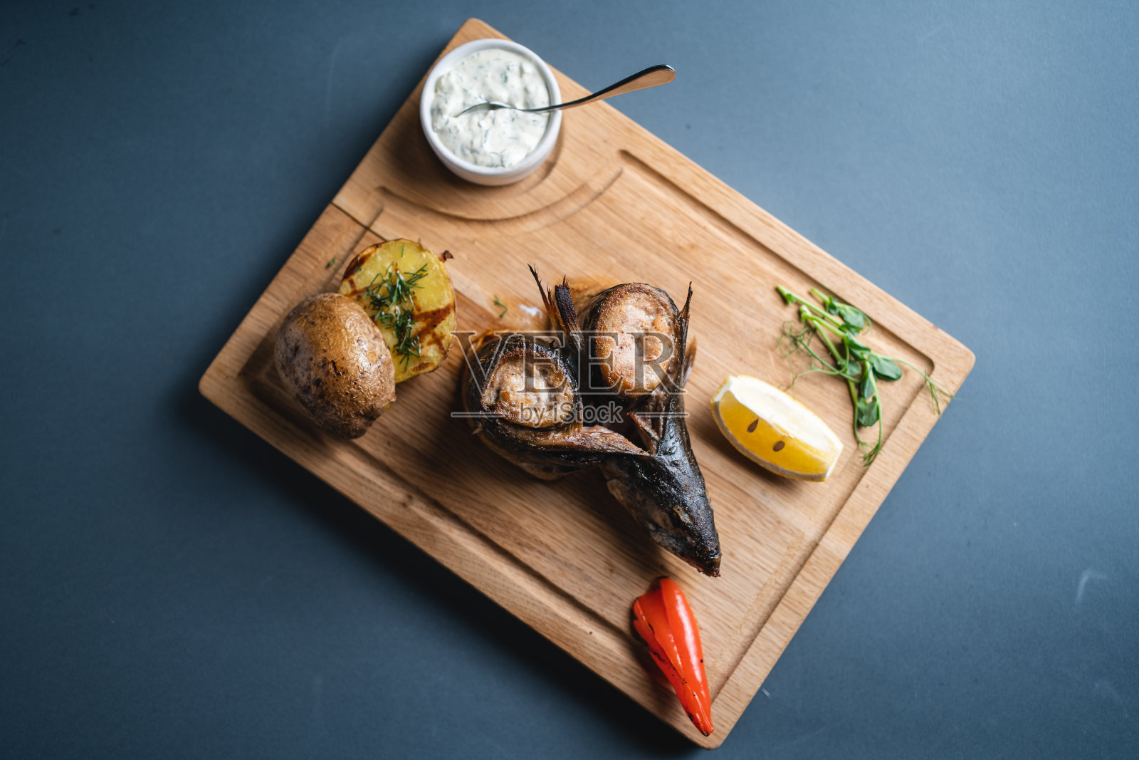 木板上的烤鲭鱼配柠檬、土豆和酱汁照片摄影图片