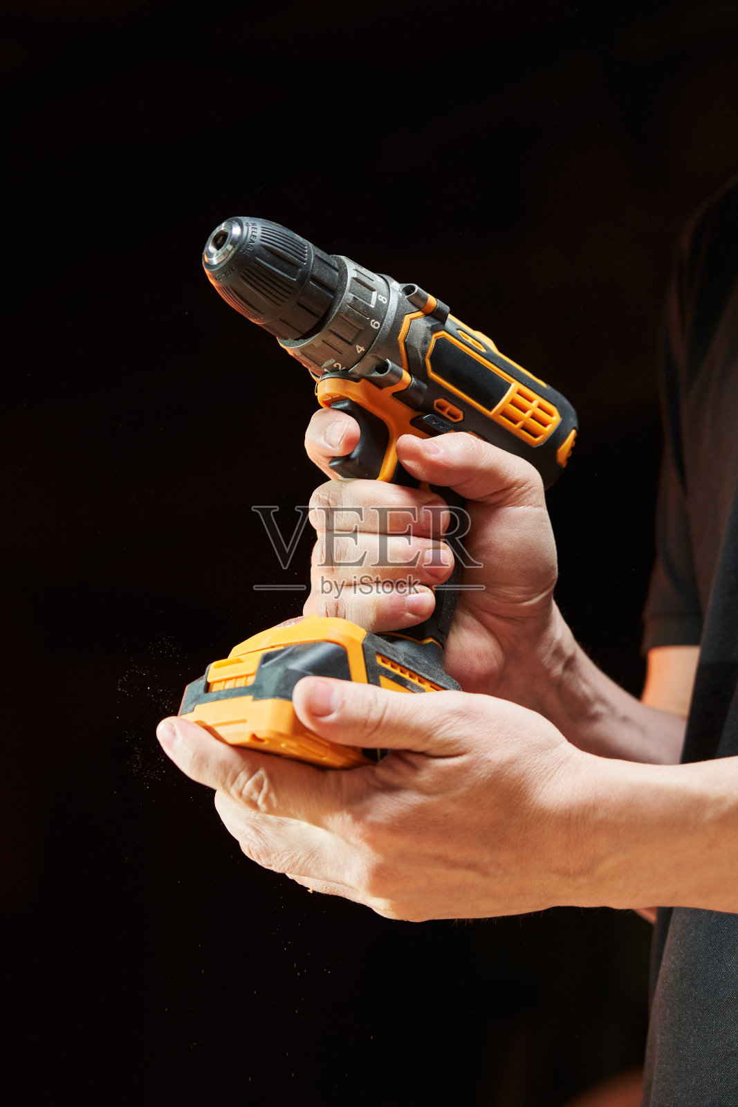 一个白人工人的手拿着一个黑色和黄色的电动螺丝刀，上面有一个可更换的电池照片摄影图片
