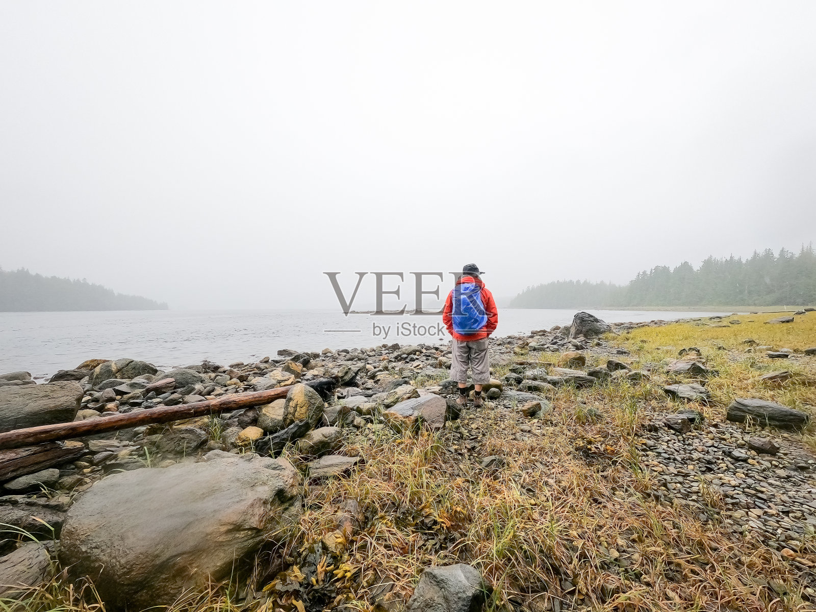 老人背包客徒步旅行在偏僻的荒野海滩，下雨天照片摄影图片