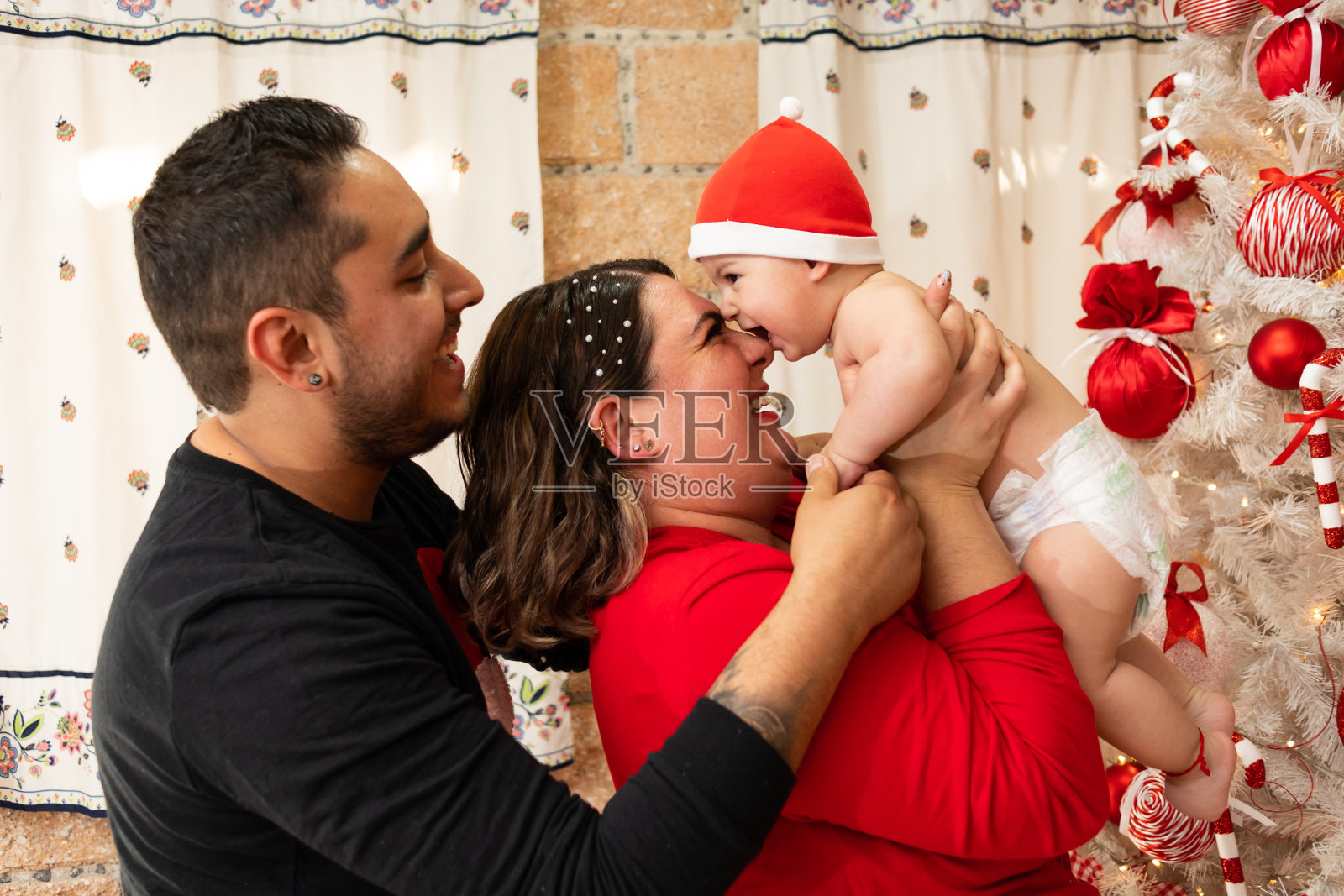 年轻活泼的西班牙家庭在客厅里玩得很开心，背景是圣诞树，拉丁父亲与高加索母亲和蹒跚学步的婴儿照片摄影图片