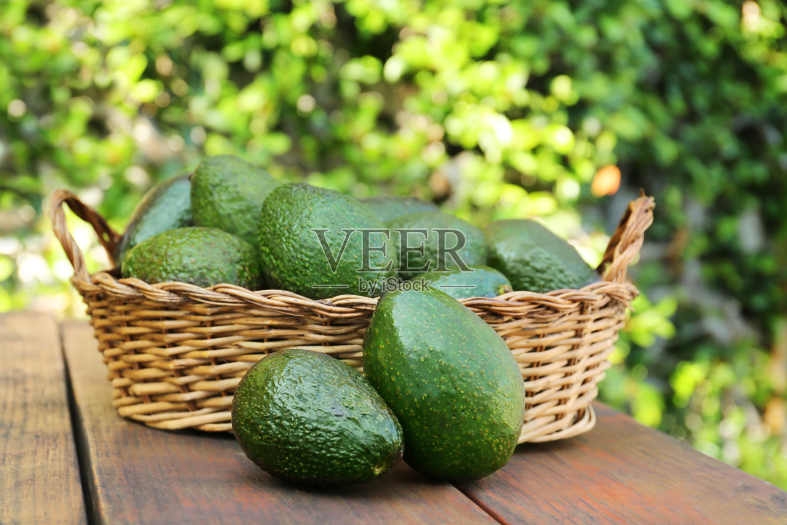户外木桌上的柳条篮子里放着新鲜成熟的牛油果照片摄影图片