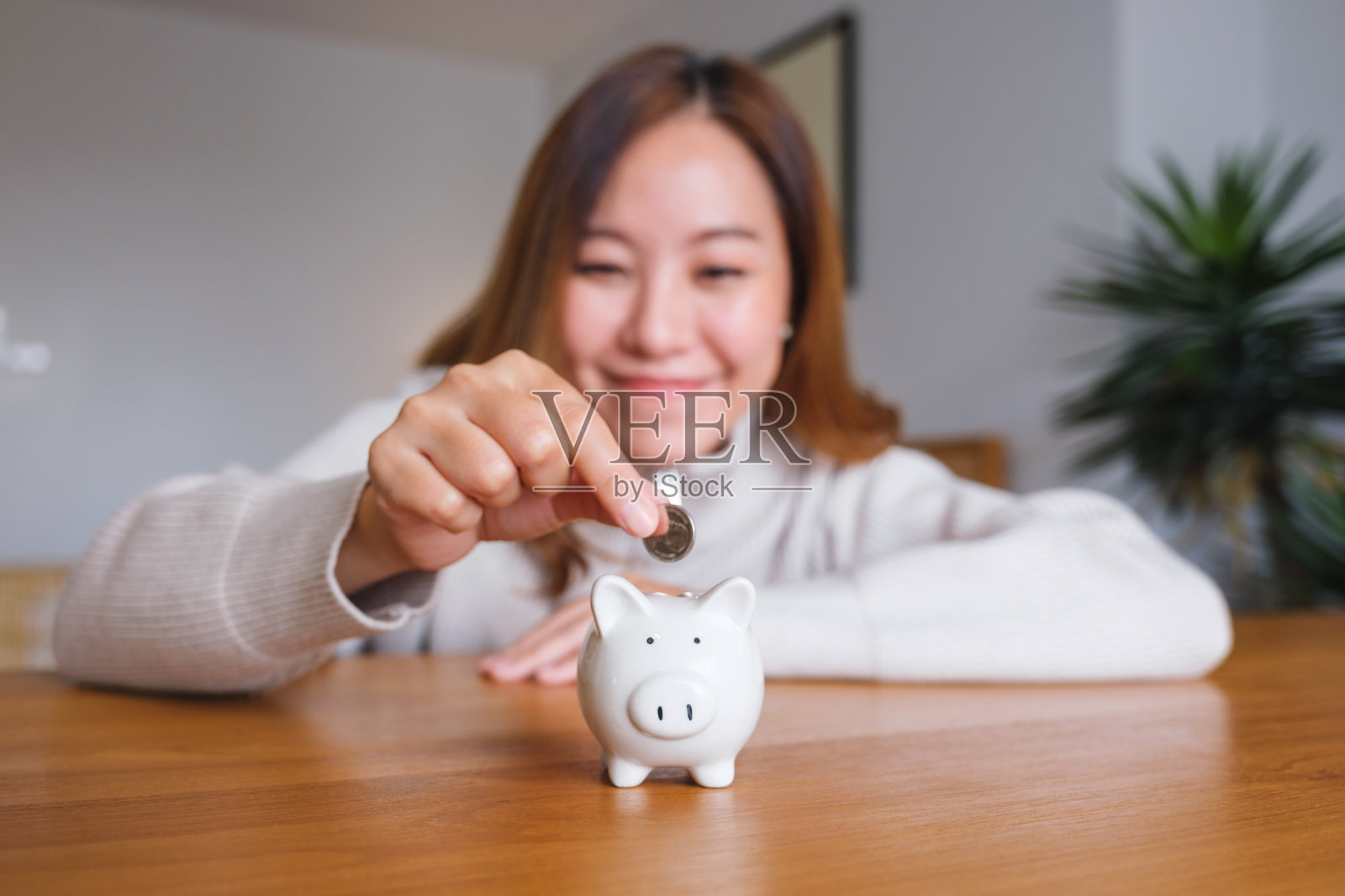 一名年轻女子手持硬币并将硬币放入存钱罐的肖像照片摄影图片