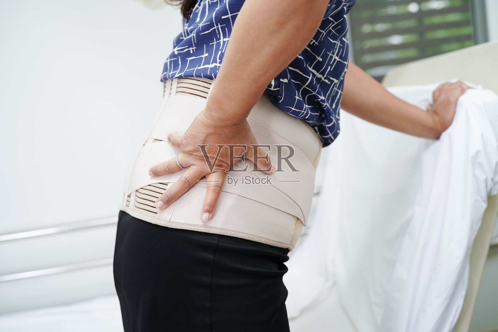 亚洲高级疼痛背部穿弹性支撑带与步行者。照片摄影图片