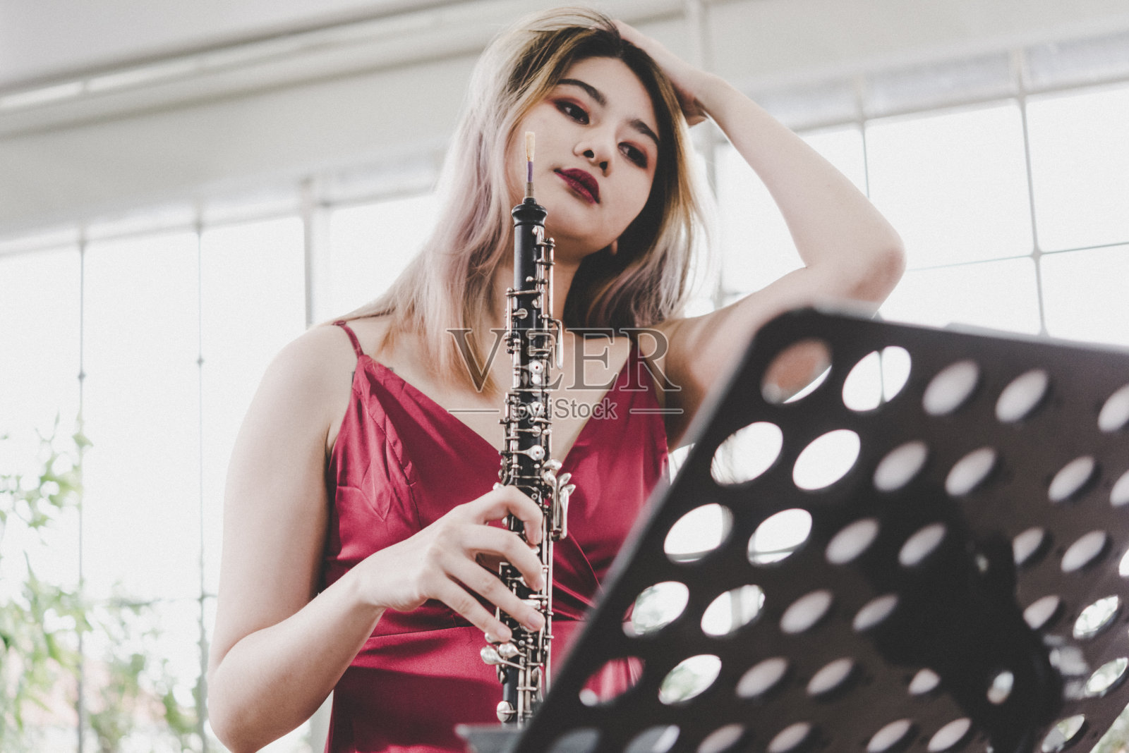 穿红裙的年轻漂亮女人正在演奏单簧管，古典音乐家正在演奏双簧管照片摄影图片