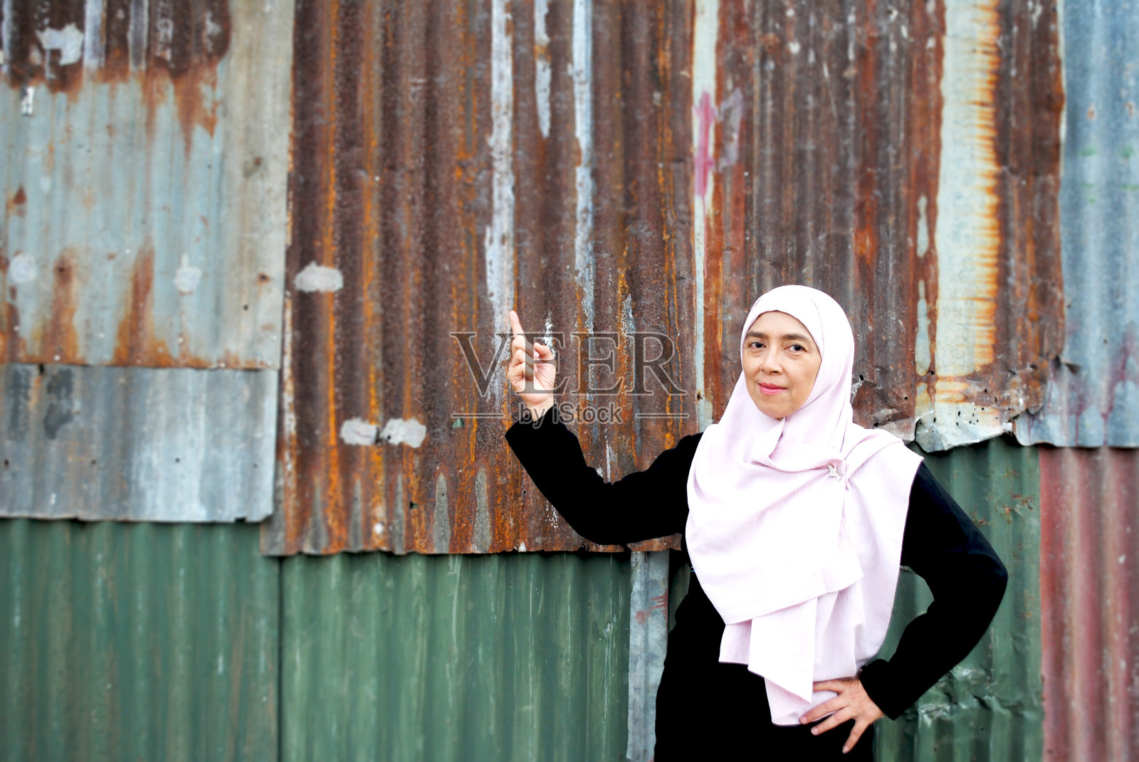 快乐的女人指着锌色背景的空白。照片摄影图片