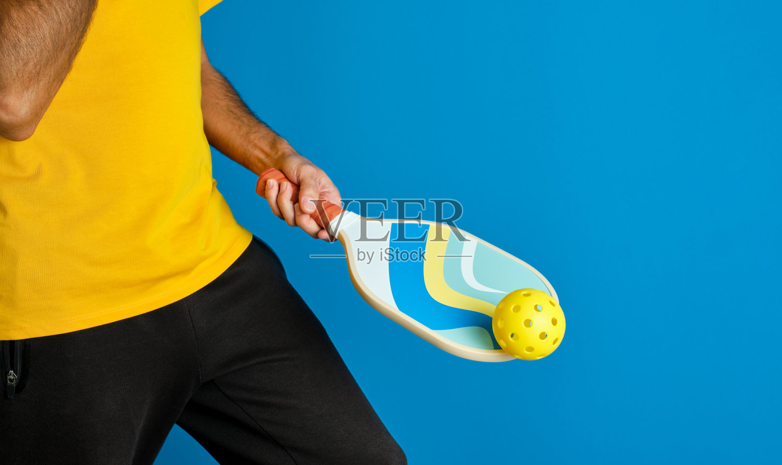 男子手里拿着蓝色的匹克球桨，蓝色背景上有一个黄色的球照片摄影图片