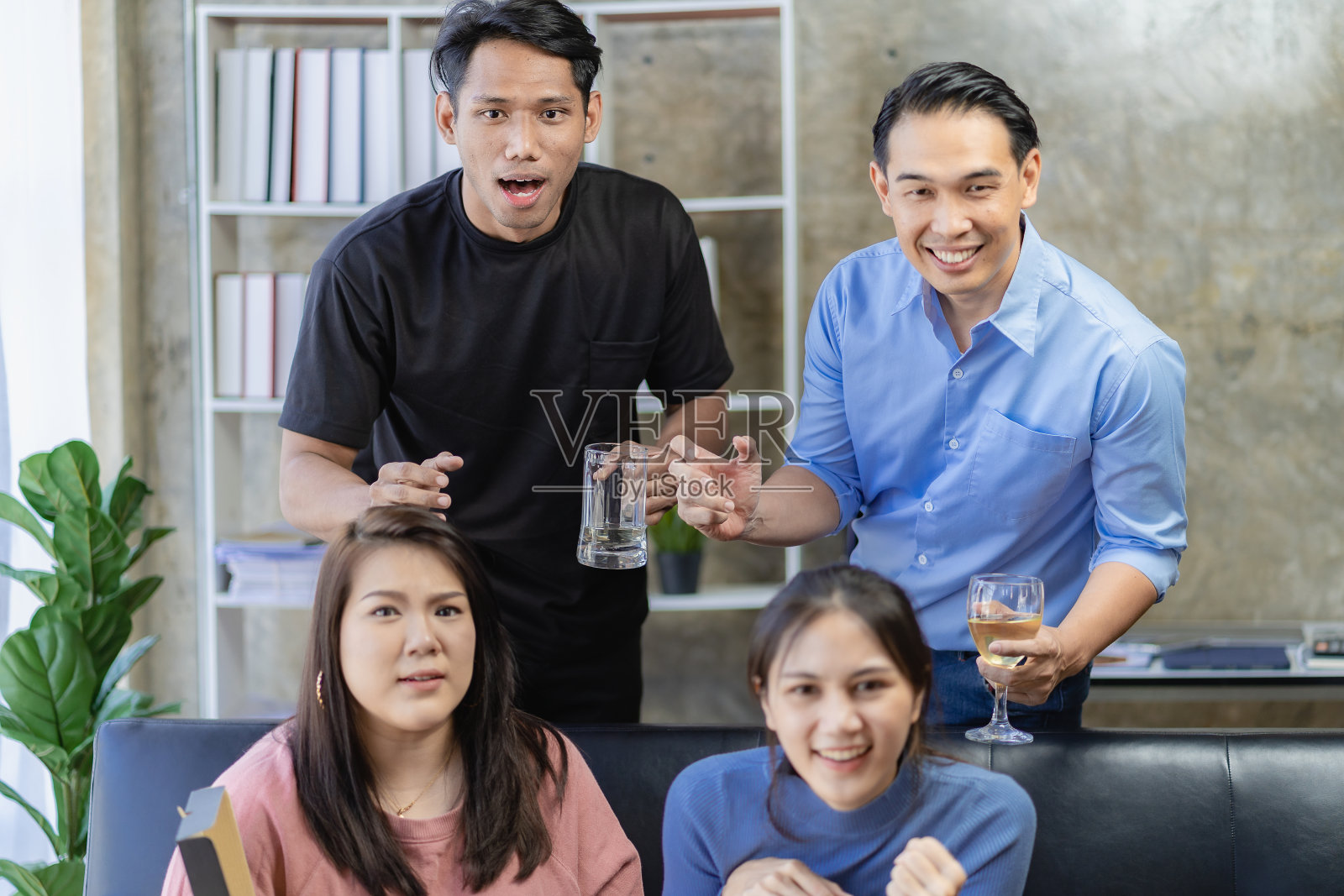 年轻的亚洲男人坐在沙发上观看和欢呼足球或足球比赛一起在家里和庆祝胜利。照片摄影图片