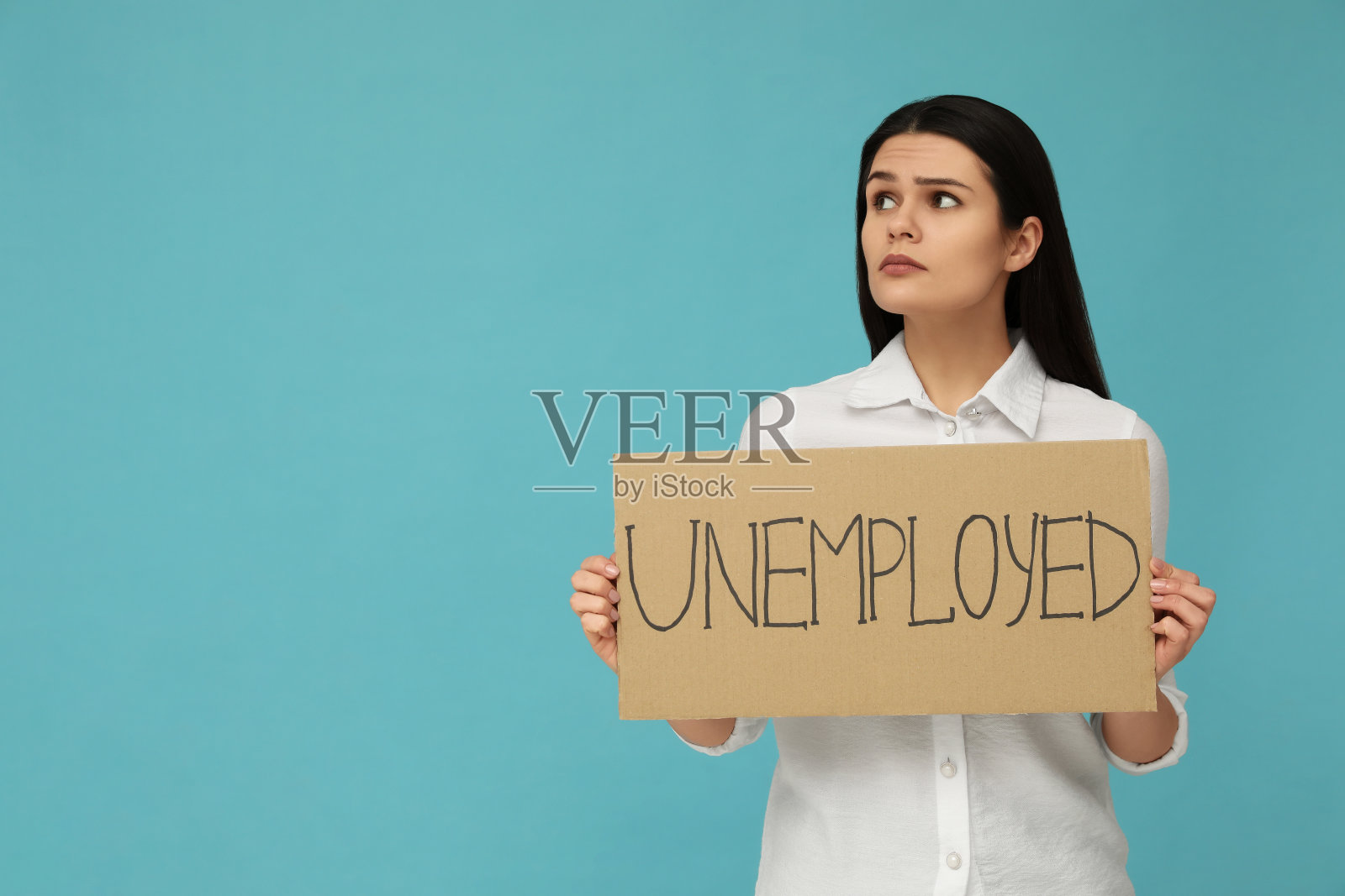 不开心的女人举着浅蓝色背景的“失业”的牌子。文本空间照片摄影图片