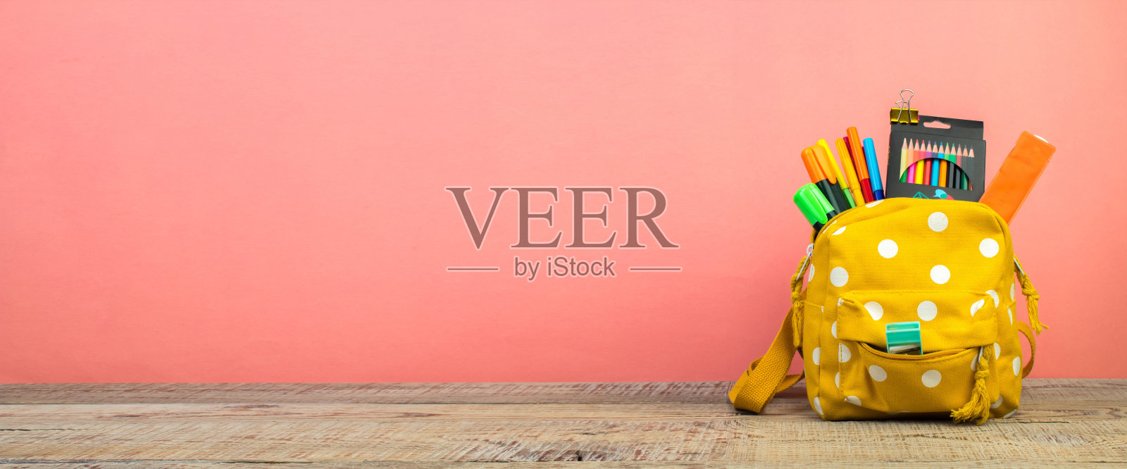 黄色背包与白色圆点与不同的彩色文具在桌子上。粉红色的背景。回到学校。横幅照片摄影图片