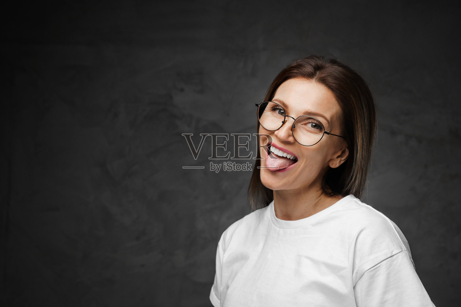 戴着眼镜，穿着白色t恤的快乐女人在黑暗的背景下微笑照片摄影图片