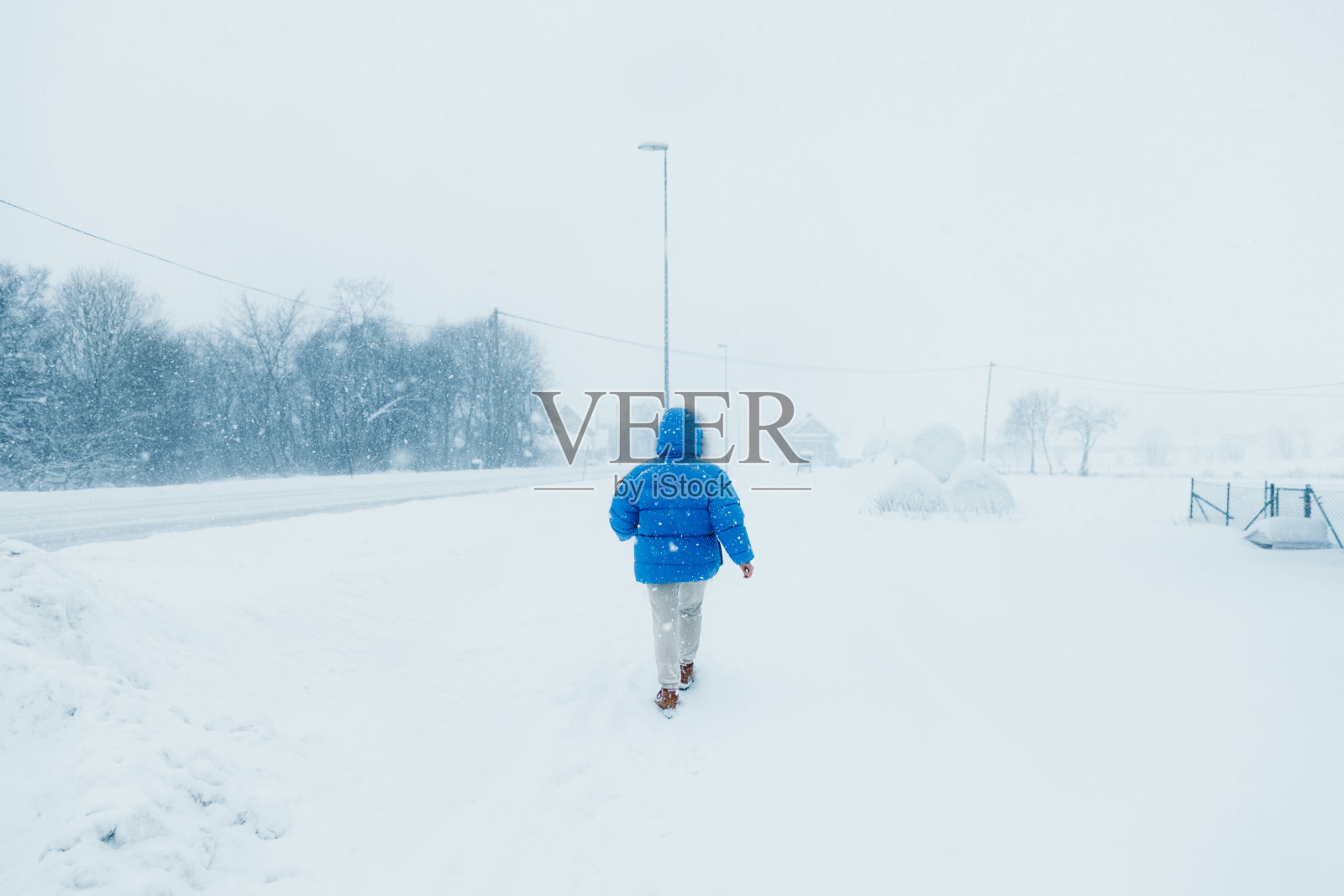 一名穿着蓝色外套的女子在大雪中漫步在斯堪的纳维亚村庄的街道上，欣赏冬天照片摄影图片