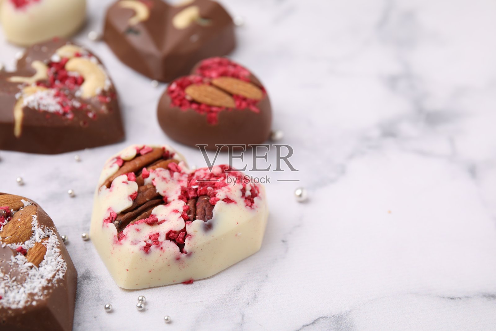 白色大理石桌子上美味的巧克力心形糖果和坚果，特写。文本空间照片摄影图片